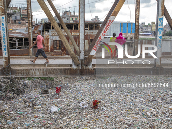Woman searches for plastic bottles to recycle from a canal full of waste in Dhaka, on September 20, 2022. Recycling is necessary because alm...