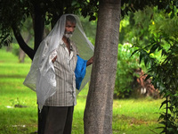 A man covers himself with a plastic sheet as he stands under a tree during a spell of rain in New Delhi, India on September 22, 2022. (