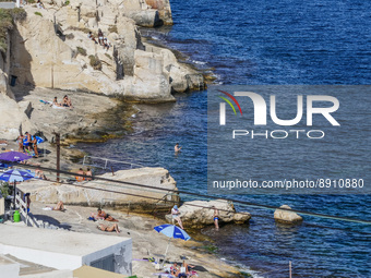 People sunbathing on the rocky beach and taking a dip and swimming in the Mediterranean Sea are seen in Valletta, Malta on 21 September 2022...