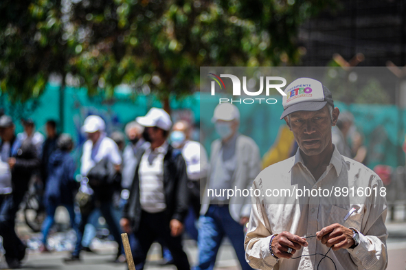 A street vendor wears a Gustavo Petro campaign cap as anti-government protesters march behind during the first antigovernment protest agains...