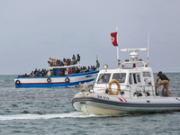A small sailboat crowded with nearly 118 people and unity of Tunisian guard watch them (
