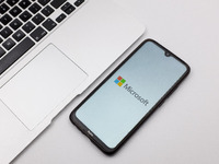 In this photo illustration a Microsoft logo seen displayed on a smartphone screen on a desk next to a Macbook in Athens, Greece on November...