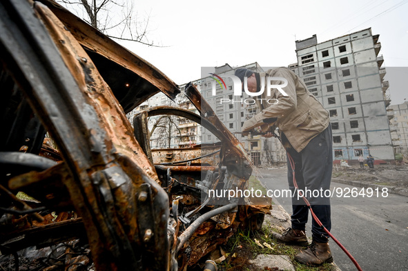ZAPORIZHZHIA, UKRAINE - NOVEMBER 22, 2022 - A man cuts a car destroyed in the shelling of Russian troops outside a ruined apartment building...