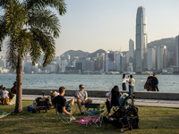 People sitting on grass at the West Kowloon Cultural District in front of the Hong Kong Skyline on December 9, 2022 in Hong Kong, China. (