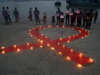 Indian volunteers and children lighting lamps on red ribbon to celebrate the  World AIDS Day on the banks of river Ganges in Kolkata , India...