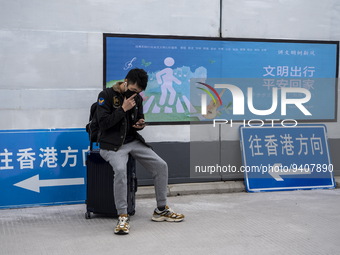 A man sitting on a suitcase next to signs pointing to Hong Kong at Shenzhen Bay Port on January 8, 2023 in Shenzhen, China. Hong Kong today...