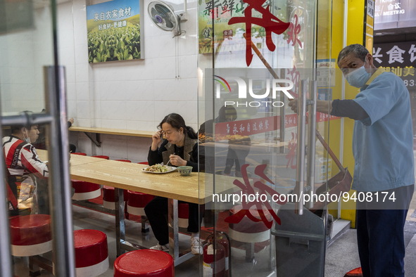 A women eating in a restaurant while a cleaner is working outside on January 8, 2023 in Shenzhen, China. China today lifts its requirement f...
