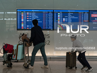 Passengers with luggages walk in front of a flight information board at Incheon International Airport on January 18, 2023, South Korea. Acco...