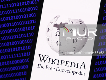 Wikipedia logo displayed on a phone screen and a binary code displayed on a screen are seen in this illustration photo taken in Krakow, Pola...