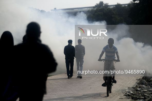 People walked past a garbage fire as it creates toxic smoke at a park area in Dhaka, Bangladesh on January 19, 2023. are burning beside a ro...