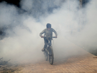 A child is seen cycling as a garbage fire creates toxic smoke at a park area in Dhaka, Bangladesh on January 19, 2023. are burning beside a...