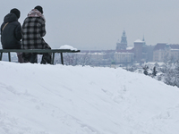 Two people are sitting on a bench near the Krakus Mound overlooking the Old Town of Krakow and Podgorze district, in Krakow, Poland, on Janu...