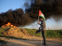 A person on crutches stands near a man waving a Palestinian flag during clashes with Israeli forces, near the Israel-Gaza border east of Gaz...