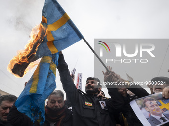 Iranian worshippers burn a national flag of Sweden as one of them holds a portrait of the French President Emmanuel Macron, in a protest aft...