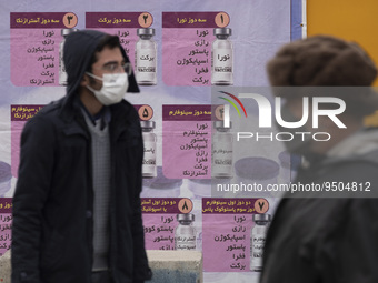 An Iranian worshipper wearing a protective face mask looks on while standing in front of a banner with Images of new coronavirus disease (CO...