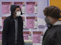 An Iranian worshipper wearing a protective face mask looks on while standing in front of a banner with Images of new coronavirus disease (CO...