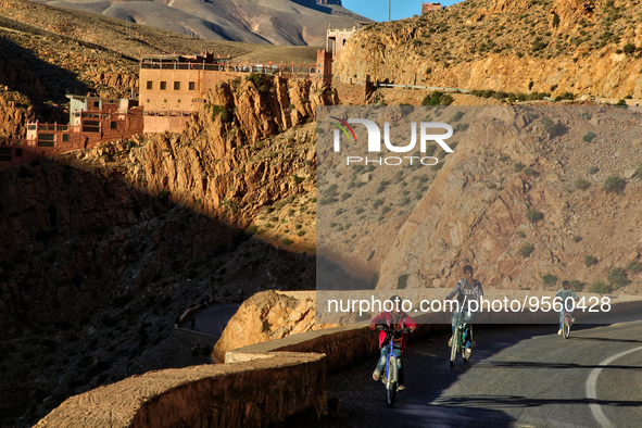 Boys ride bicycles along a road winding through the Dades Gorge in the Dades Valley deep in the High Atlas Mountains in Dades, Morocco, Afri...