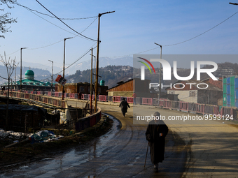 People walk early morning on a bridge as a Mosque (Masjid) is seen in Baramulla Jammu and Kashmir India on 15 February 2023 (