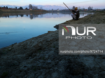 A kashmiri man sits on the banks of river Jehlum to catch fish in Sopore District Baramulla Jammu and Kashmir India 10 March 2023 (