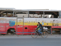 A Syrian man rides a bicycle  past a damaged bus in the Al-Sakhour neighbourhood of Aleppo on December 24, 2015. The graffiti on the bus rea...