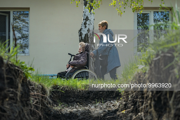 A woman in wheelchair with her daughter pass near the entrance of a improvised underground shelter against shelling after receiving medical...