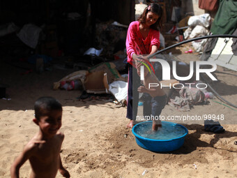 Palestinian Bedouin girl washes her brother with water outside her family's hut in Gaza City, on May 4, 2014. (