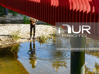 Young Man By Stream Under Red Bridge