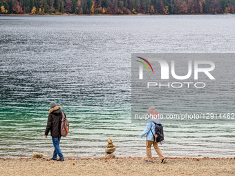 Hikers Walk Along Eibsee Shoreline Under Cloudy Autumn Sky