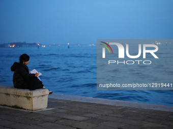 Young Woman Writing On Seawall Bench Overlooking Venetian Lagoon At Blue Hour