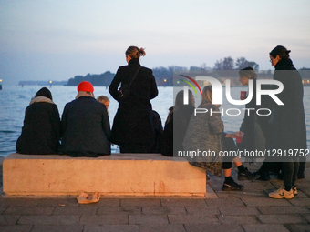 Group Of Young Women Gather On Seawall Bench By Venetian Lagoon At Dusk