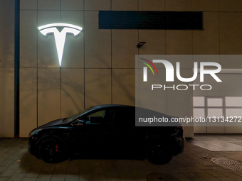 TESLA Logo At Night Above A Parked Electric Tesla Car