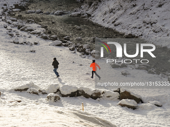 Children Playing On Snowy Banks Of A Stream In The Bavarian Alps