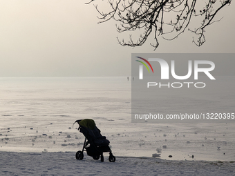 Two People On Frozen Lake And Baby Stroller Visible Along The Lakeshore