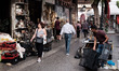 People are walking in front of a store while a man is working in the center of Athens, Gre...
