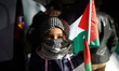 A young girl wears a keffieh and holds Palestinian flags. Thousands of people desmonstrate...