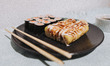 Banana sushi rolls and salmon maki sushi rolls are sitting on a plate next to two glasses...