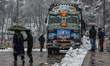 People are walking as a truck is parked on a bridge amid snowfall in Baramulla, Jammu and...