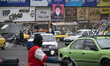 Vehicles are driving past an electoral banner featuring a portrait of Iran's Supreme Leade...