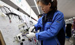 A worker is producing automotive wiring harness products at a workshop of an auto parts ma...
