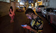 A young Iranian man is checking his social media pages on his cellphone while standing in...