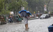 A street vendor is carrying clothes as he wades through a waterlogged road during rainfall...