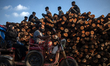 A battery-run autorickshaw is driving past tree logs where boys are sitting near the Burig...