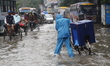 A delivery man is walking through a waterlogged street during heavy rainfall in Dhaka, Ban...