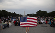 A person is holding the US flag as he is waiting for fireworks to celebrate US Independenc...