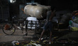 A laborer unloads sacks filled with aluminum utensils from a cycle rickshaw along a roadsi...