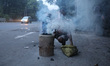 A roadside food vendor lights a coal oven before starting his business during the early mo...