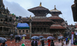 People with umbrellas walk around Patan Durbar Square, a UNESCO World Heritage Site in Lal...