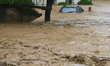 A man wades through the flooded river to reach his partially submerged car in Lalitpur, Ne...