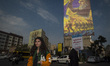 A young Iranian woman who does not wear a mandatory headscarf walks under a giant banner f...