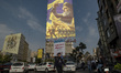 A young Iranian man walks under a giant banner featuring a portrait of Lebanon's Hezbollah...